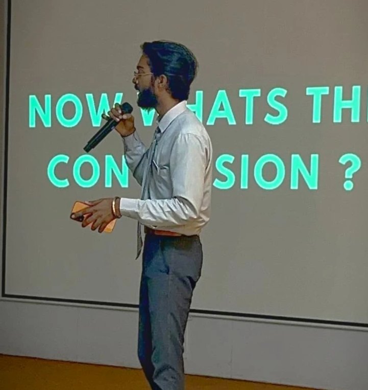 Pranjul Rathour presenting with a microphone in front of a slide reading 'Now what's the conclusion?'